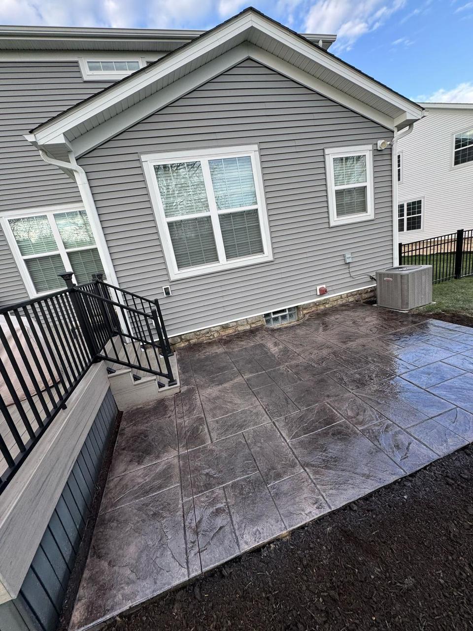 Grey slate stamped concrete patio alongside a deck and stairs