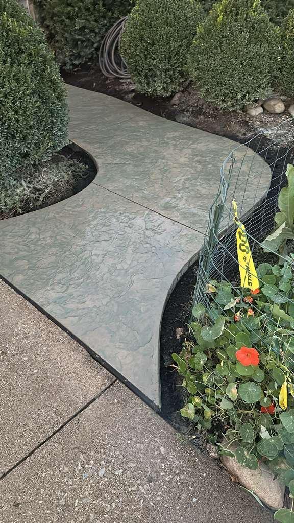 Curved stamped concrete walkway through a garden bed